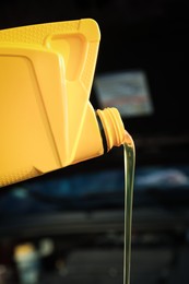 Photo of Pouring motor oil from yellow container on blurred background, closeup