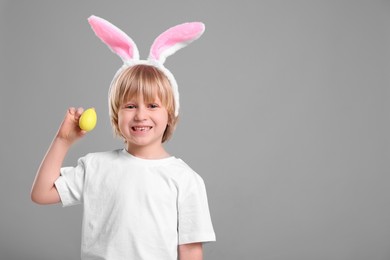 Photo of Happy boy in bunny ears headband holding painted Easter egg on grey background. Space for text