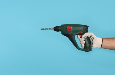 Worker in gloves with power drill on light blue background, closeup. Space for text