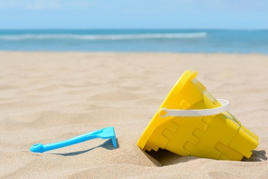 Plastic bucket and rake on sand near sea, space for text. Beach toys