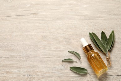 Bottle of essential sage oil and plant leaves on wooden table, flat lay. Space for text
