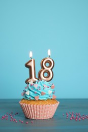 18th birthday. Delicious cupcake with number shaped candles for coming of age party on light blue wooden table