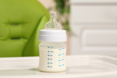 Photo of High chair with feeding bottle of infant formula on white tray indoors
