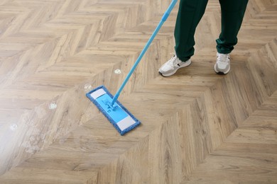 Professional janitor cleaning parquet floor with mop, closeup