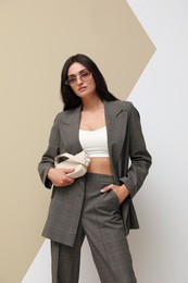 Beautiful woman with sunglasses and bag in formal suit on color background. Business attire