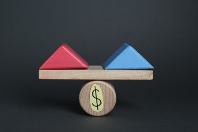 Photo of Gender pay gap. Wooden triangles as male and female symbols on miniature seesaw against black background