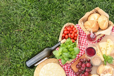 Picnic blanket with wine and food on green grass, top view