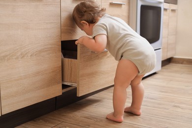 Little child exploring drawer in kitchen. Dangerous situation