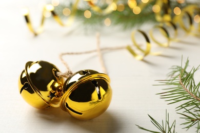 Golden sleigh bells and fir branch on white table, closeup