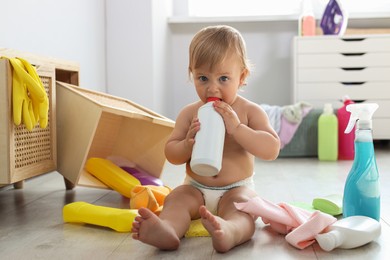 Photo of Cute baby playing with bottle of detergent on floor at home. Dangerous situation