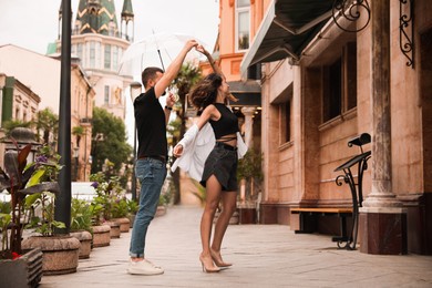 Photo of Young couple with umbrella dancing under rain on city street