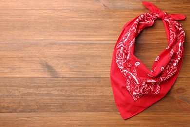 Tied red bandana with paisley pattern on wooden table, top view. Space for text