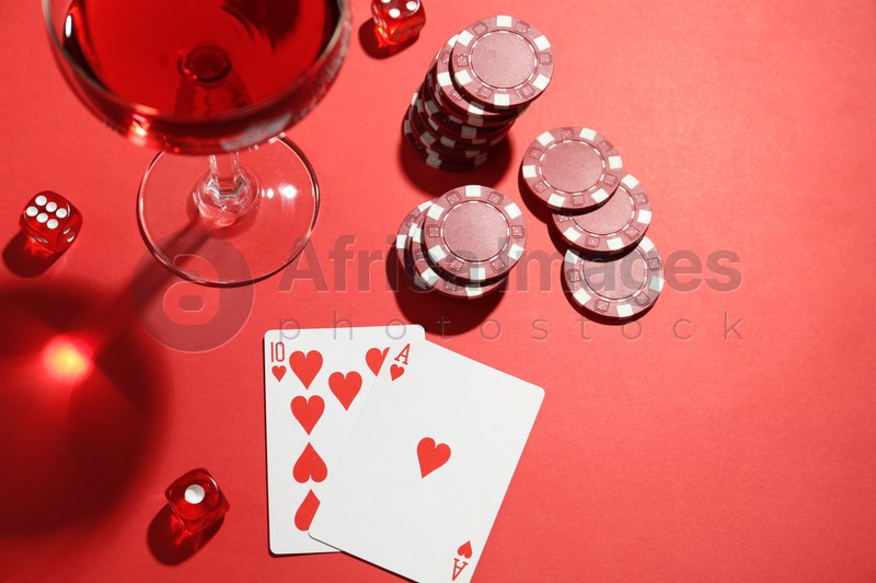 Casino chips, playing cards, dice and cocktail on red  table, flat lay