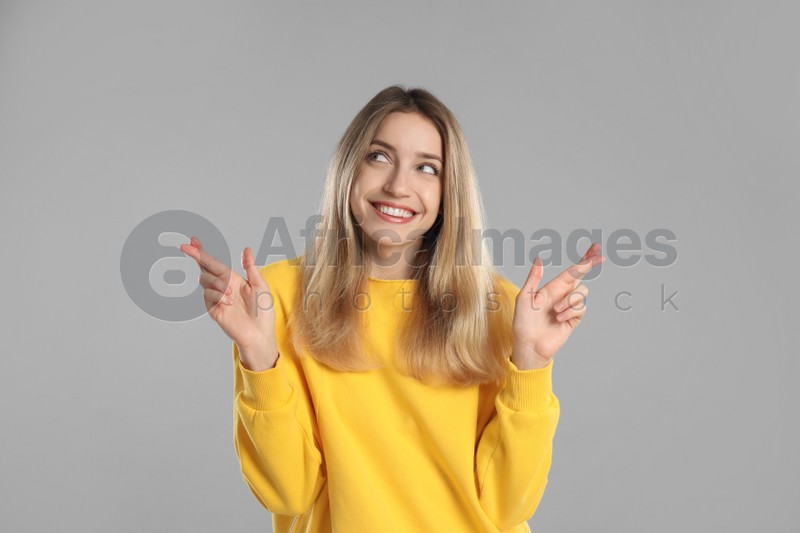 Woman with crossed fingers on light grey background. Superstition concept