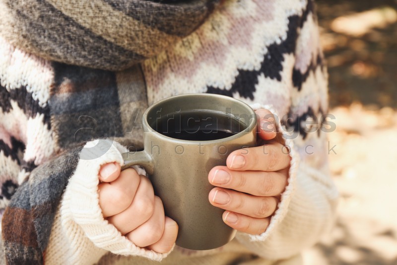 Woman in cozy sweater with cup of hot drink outdoors on sunny autumn day, closeup