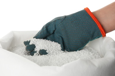 Man taking pellets of ammonium nitrate from sack on white background, closeup. Mineral fertilizer