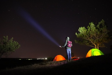 Man with bright flashlight near camping tents outdoors at night