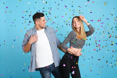 Happy couple and falling confetti on light blue background
