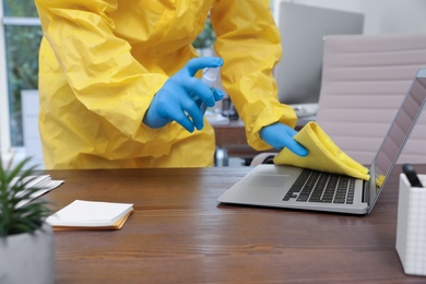 Janitor disinfecting laptop in office to prevent spreading of COVID-19