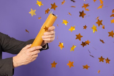 Photo of Man blowing up party popper on purple background, closeup