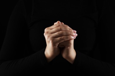 Woman holding hands clasped while praying in darkness, closeup