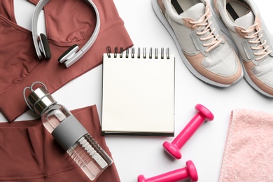 Flat lay composition with sportswear, notebook and dumbbells on white background. Gym workout plan