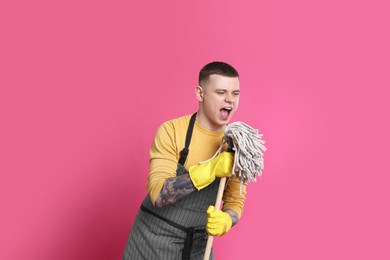 Handsome young man with mop singing on pink background. Space for text