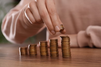 Woman stacking coins at wooden table indoors, closeup