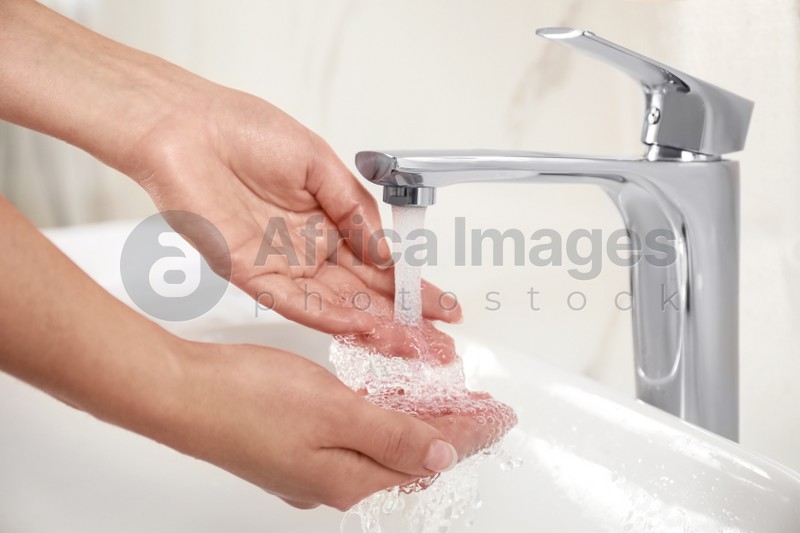 Young woman washing hands over sink in bathroom, closeup