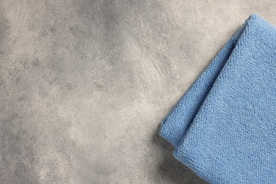 Photo of Soft folded terry towel on light gray textured background, top view. Space for text