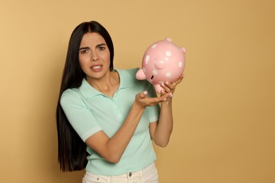 Photo of Young woman with ceramic piggy bank on beige background