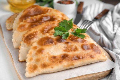Board with delicious fried chebureki and parsley on white table, closeup