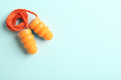 Pair of orange ear plugs with cord on turquoise background, top view. Space for text