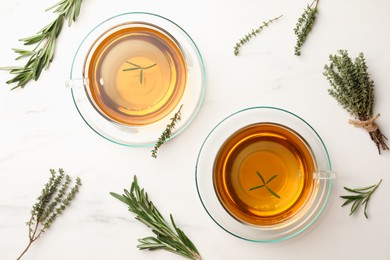 Cups of aromatic herbal tea with thyme and rosemary on white marble table, flat lay