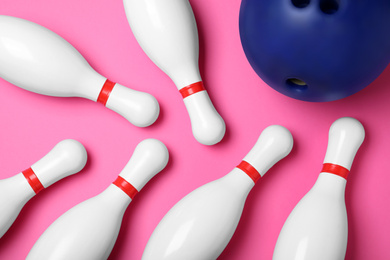 Bowling ball and pins on pink background, flat lay