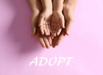 Mother holding hands with her child on pink background, top view. Adoption concept