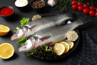 Photo of Fresh raw sea bass fish and ingredients on black table