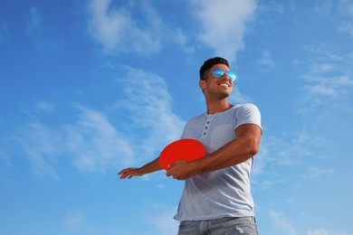Happy man throwing flying disk against blue sky on sunny day, low angle view