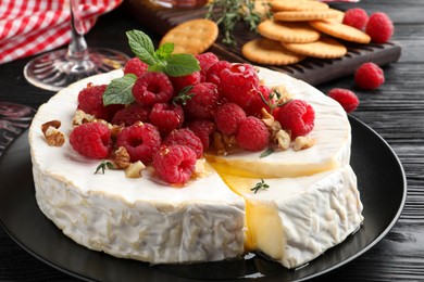 Brie cheese served with raspberries and walnuts on black wooden table, closeup
