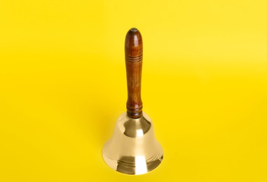 Golden school bell with wooden handle on yellow background