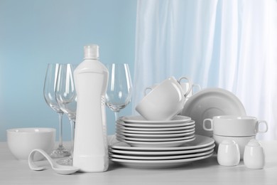 Photo of Clean dishware and bottle of detergent on light grey table