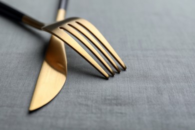 Golden fork and knife on grey table, closeup. Space for text
