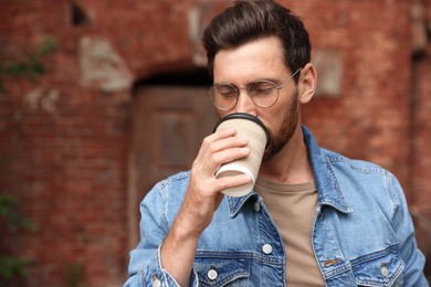 Photo of Handsome bearded man drinking from paper cup outdoors. Space for text