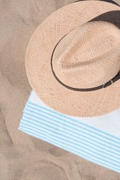 Straw hat and beach towel on sand, top view