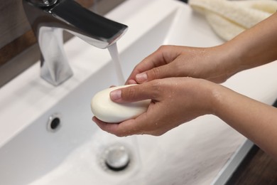 Photo of Woman with soap bar washing hands in sink, closeup