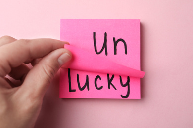 Woman holding notes with word UNLUCKY on pink background, top view