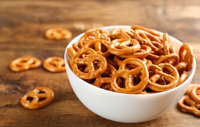 Bowl with delicious pretzel crackers on wooden table, closeup