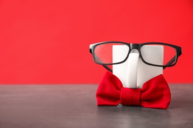 Funny composition with bow tie, glasses and cup on grey table against red background. Space for text
