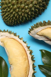 Fresh ripe durians and leaves on light blue background, flat lay