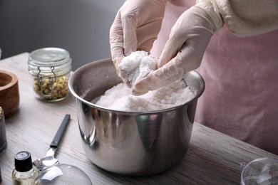 Photo of Woman in gloves making bath bomb mixture at wooden table, closeup
